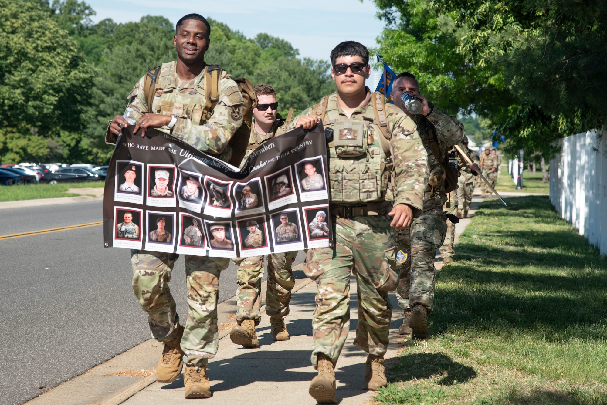 U.S. Airmen from the 316th Security Forces Group carry a poster memorializing 14 defenders killed in combat during the 5-kilometer Fallen Defender Ruck at Joint Base Andrews, Md., May 12, 2025. Midway through the ruck, Airmen honored those security forces members by completing a pushup for each fallen member. (U.S. Air Force photo by Patrick Griffith)