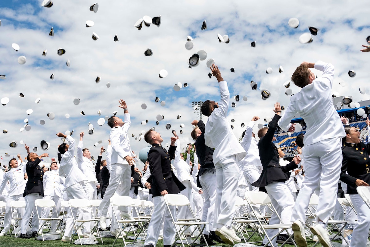 U.S. Naval Academy graduates toss their caps in the air outdoors en masse.