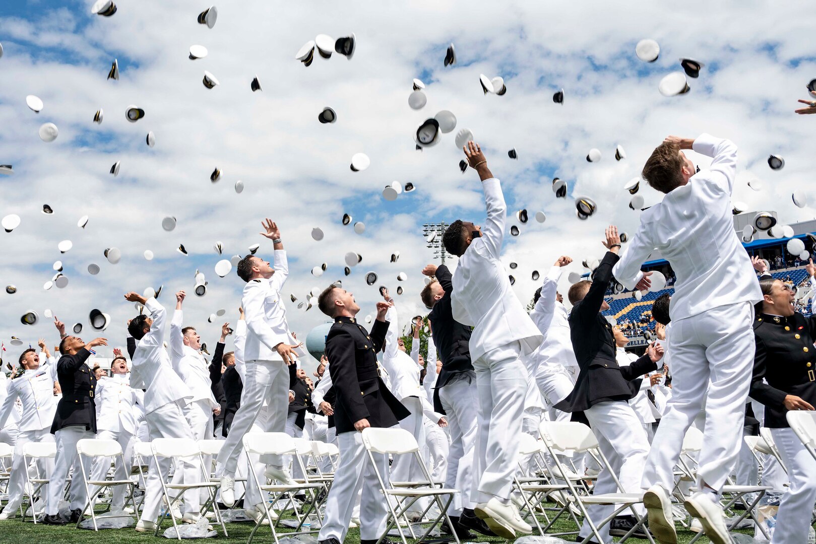 U.S. Naval Academy graduates toss their caps in the air outdoors en masse.