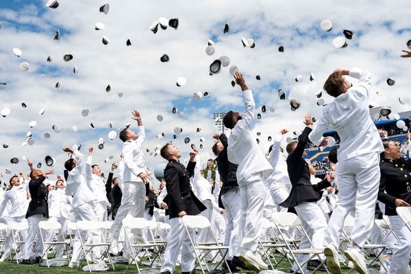 U.S. Naval Academy graduates toss their caps in the air outdoors en masse.