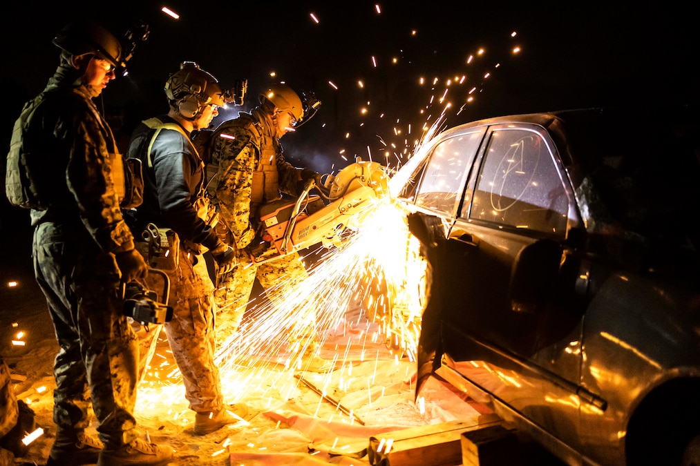 Sparks fly as a Marine cuts into a vehicle with a large circular saw and two others look on.