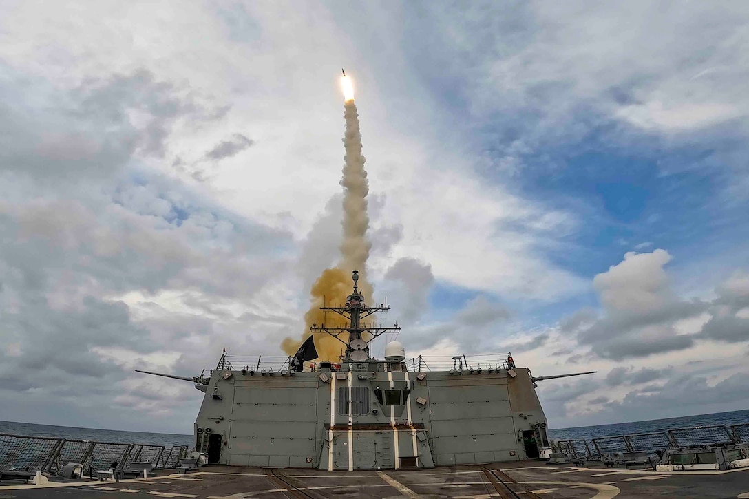 A missile fires from a ship toward a cloudy sky in the open ocean.