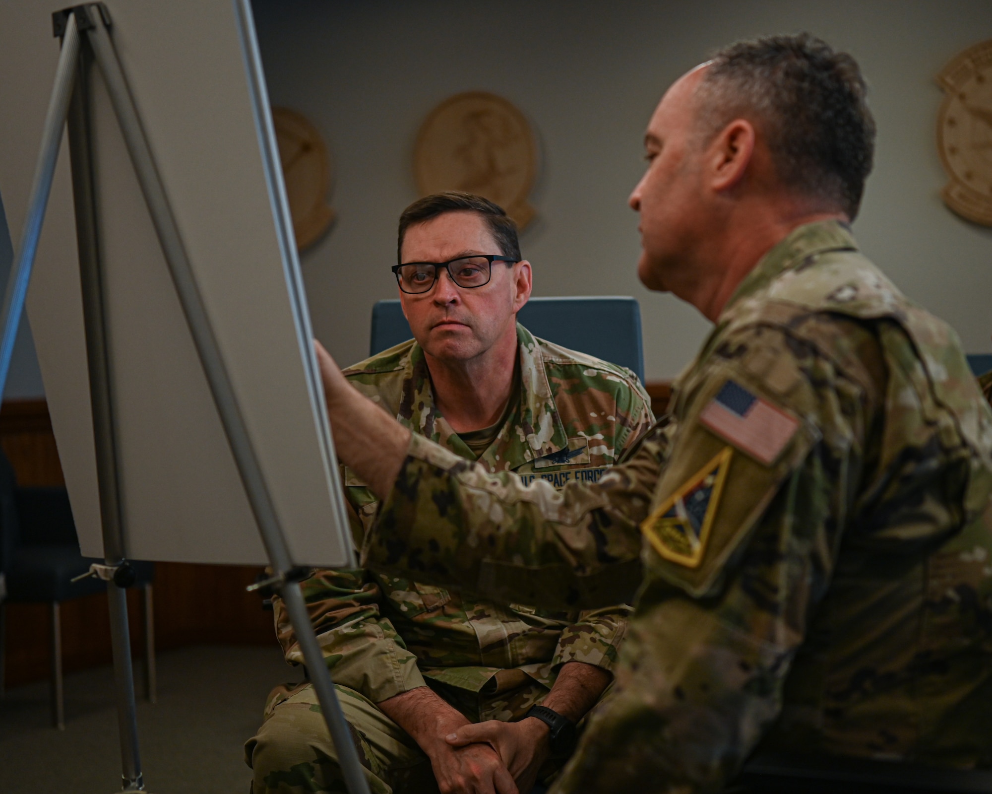 U.S. Space Force Col. Mark Shoemaker, Space Launch Delta 30 commander, right, briefs U.S. Space Force Chief of Space Operations Gen. Chance Saltzman, left, on current and future mission objectives using a demonstration board in the headquarters office at Vandenberg Space Force Base.