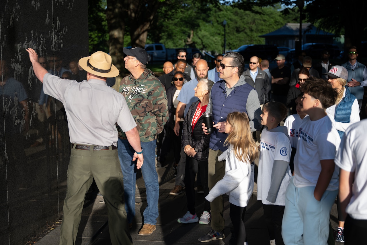 The defense secretary and volunteers stand in front of a memorial.