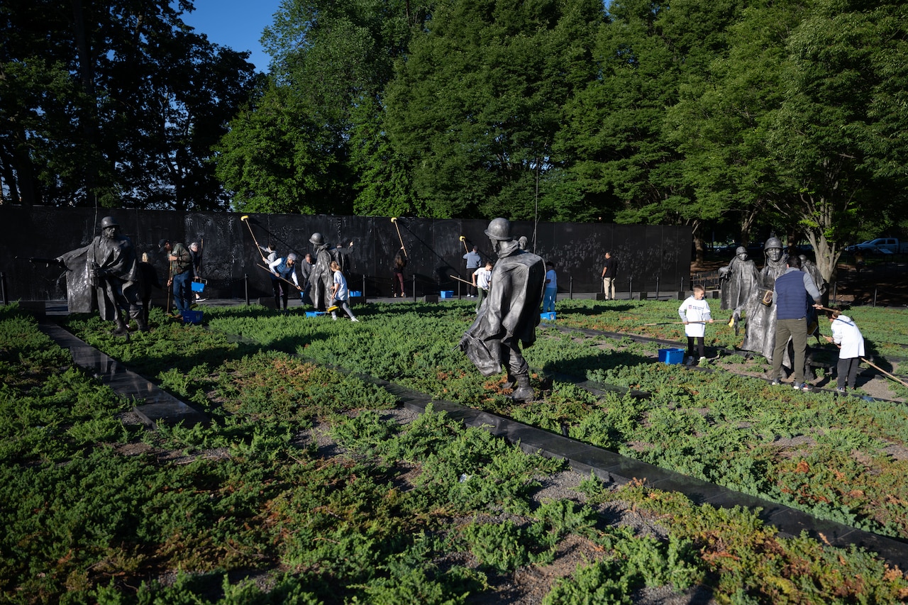 The defense secretary and volunteers clean statues.