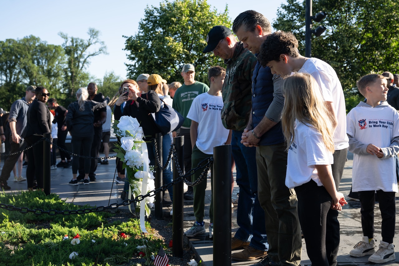 The defense secretary and another bow their heads in front of a wreat at a memorial.