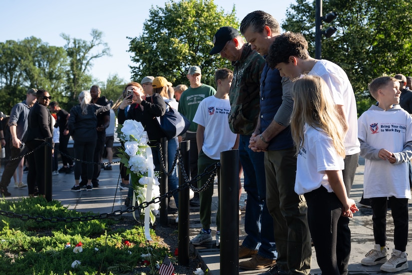 The defense secretary and another bow their heads in front of a wreat at a memorial.