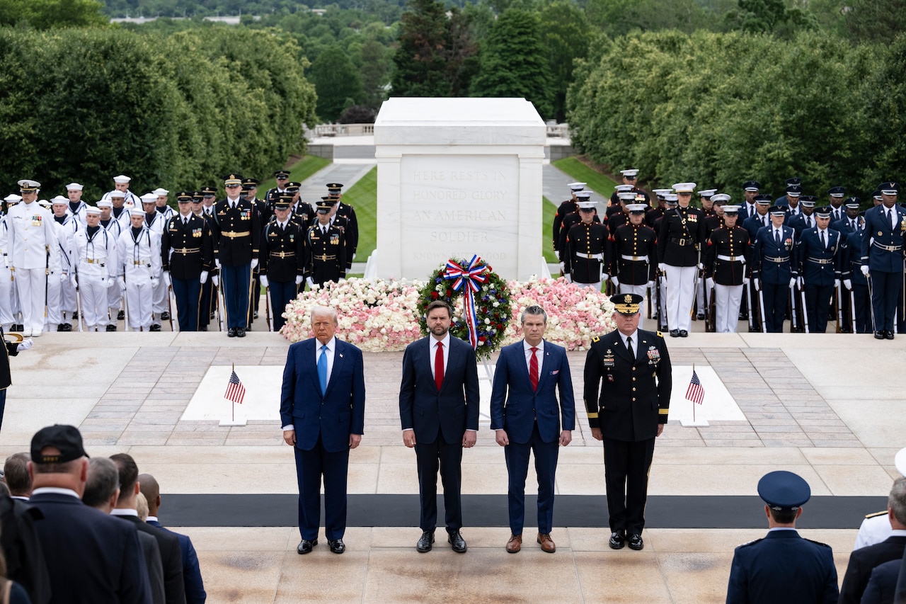 Four men stand next to each other in front of wreath during a ceremony.