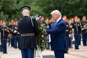 The president touches a wreath during a ceremony as fellow service members in formation watch from the background.