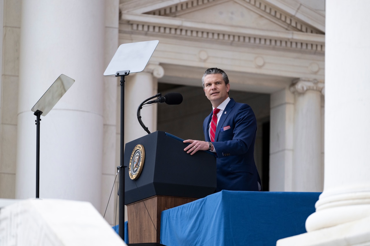 The defense secretary speaks on a stage in front of an American flag.
