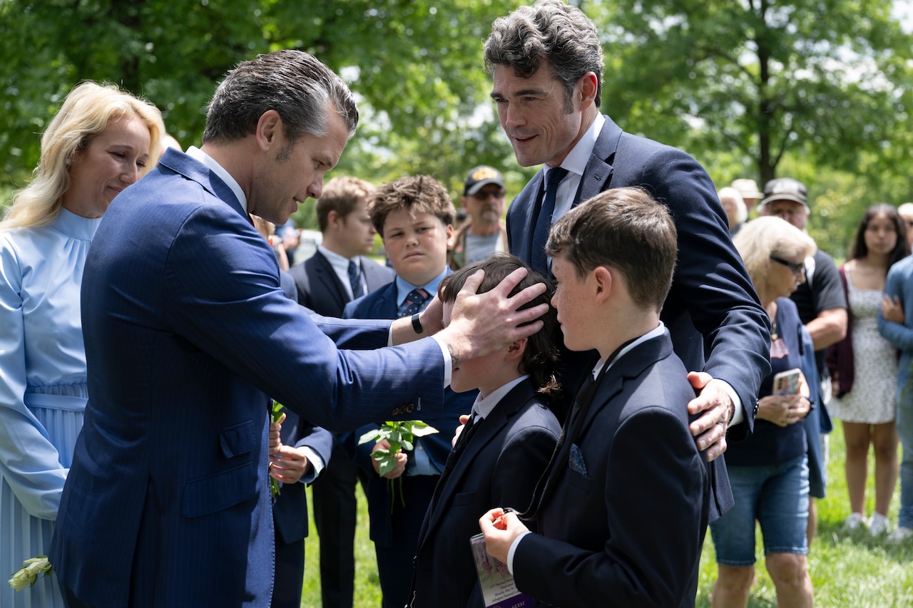 The defense secretary puts his hand on a child's head as other children stand nearby as two adults watch.