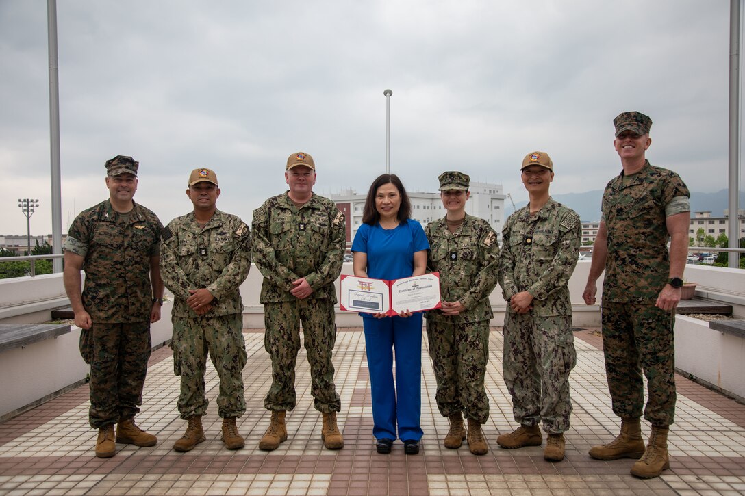 U.S. Marine Corps Col. Richard Rusnok, left, the commanding officer of Marine Corps Air Station Iwakuni, and a Pennsylvania native, Sgt. Maj. Steven Kern, right, the sergeant major of Headquarters & Headquarters Squadron, MCAS Iwakuni, and an Ohio native, and Marde D Buchart, center, a radiologic technician (mammographer) with Naval Hospital Yokosuka Japan, pose for a group photo with the leadership of MCAS Iwakuni Naval Family Branch Clinic during the May 2025 Impact Iwakuni award ceremony at MCAS Iwakuni, Japan, May 21, 2025. The Impact Iwakuni award is presented monthly to recipients that make a significant positive impact on the and Marde D Buchart won the award for her outstanding support of the MCAS Iwakuni Naval Family Branch Clinic while operating as the sole Mammographer since August 2024. (U.S. Marine Corps photo by Sgt. Randall Whiteman)
