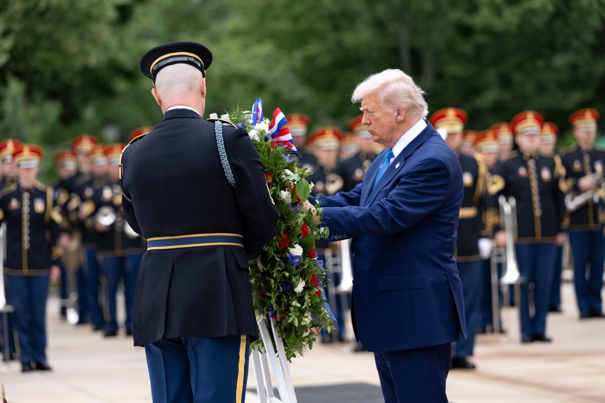 The president touches a wreath during a ceremony as fellow service members in formation watch from the background.