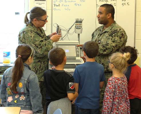 Hospital Corpsman First Class (HM1) Sandra Zdunowski, discusses the essential role of properly maintaining medical equipment in saving lives. Zdunowksi is a biomedical technician at NMRTC Patuxent River and brought an EKG machine to the career fair, engaging students with a glimpse into the world of medical technology. Zdunowski emphasized the constant challenge of keeping medical equipment operational, especially in the mobile and demanding combat environments faced by Navy personnel, whether supporting Marines on land or Sailors at sea. Hospital Corpsman Second Class (HM2) Luis Morales looks on as the students ask questions.