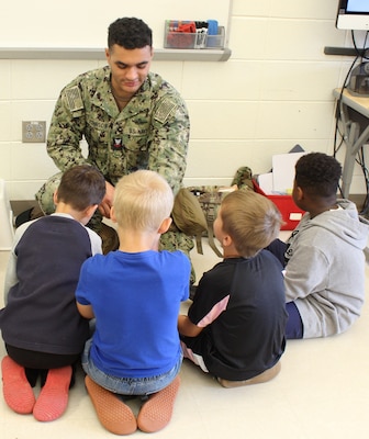 Hospital Corpsman Second Class (HM2) Ethan Johnson utilized training equipment from Tactical Combat Casualty Care (TCCC) to demonstrate wound packing and bandaging techniques. He provided a brief overview of TCCC and the critical role corpsmen play in stabilizing Marines and Sailors in combat situations until they are transported for more advanced medical care. Students watch HM2 Johnson as he packs a simulated wound.