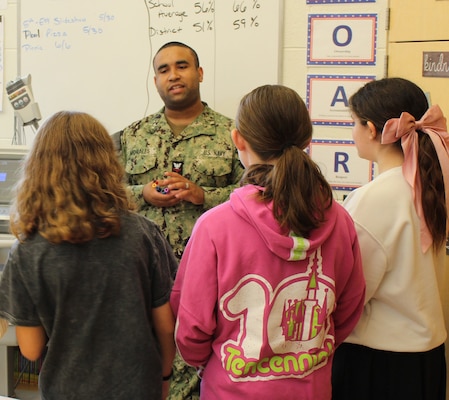 Hospital Corpsman Second Class (HM2) Luis Morales, Laboratory Technician, captivated students with examples of germs and bacteria viewed under a microscope, discussing the intricacies and importance of laboratory work in diagnosing and monitoring patient health. He touched on the variety of specimens analyzed in the lab, including blood, urine, and other bodily fluids. The conversation with HM2 Morales sparked a lively exchange as several students shared their personal experiences of providing blood and other lab specimens, creating a relatable connection and highlighting the role the lab plays in their own healthcare journeys.