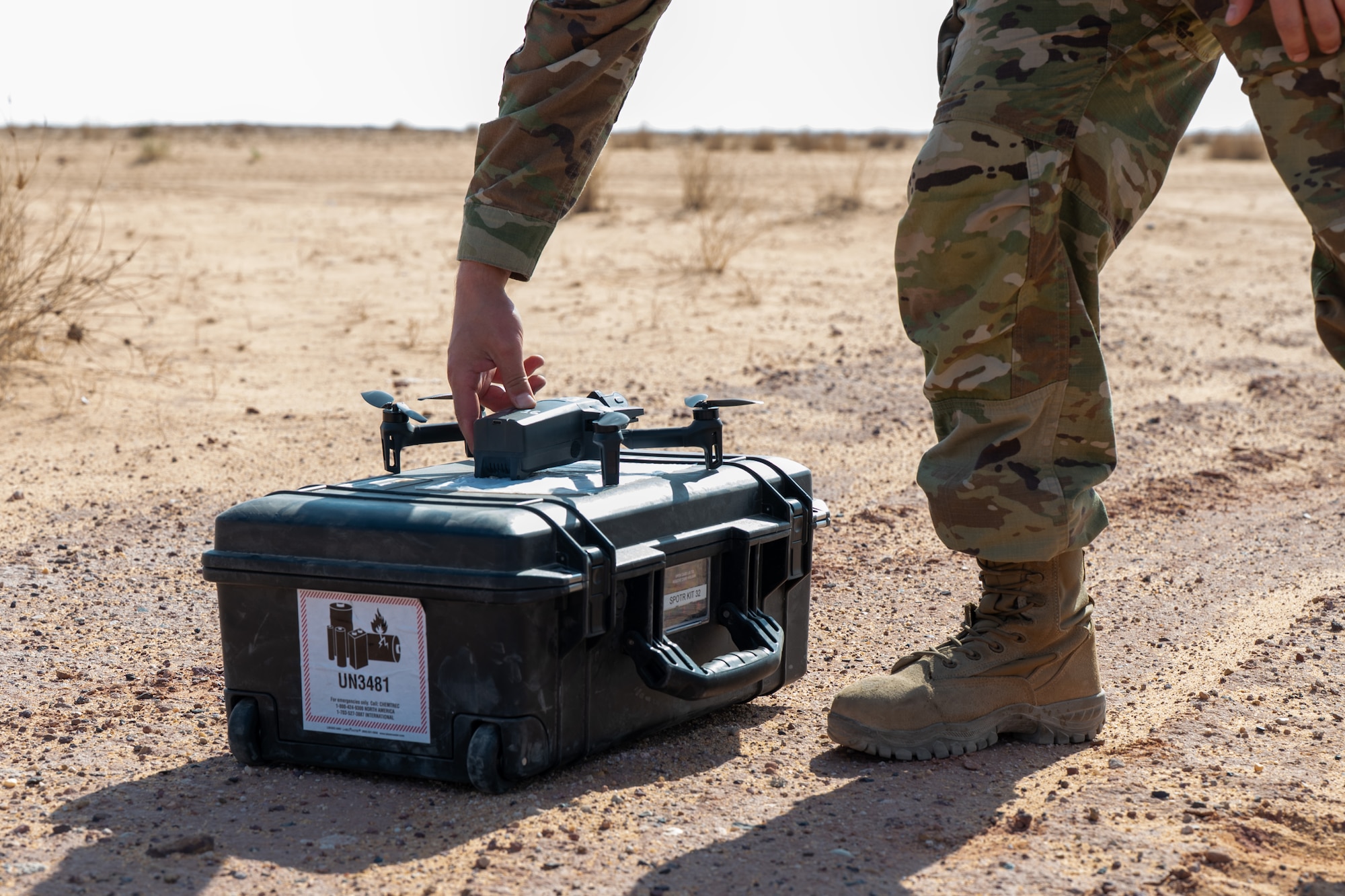 Airman powers on a drone sitting on a Pelican Case in the desert