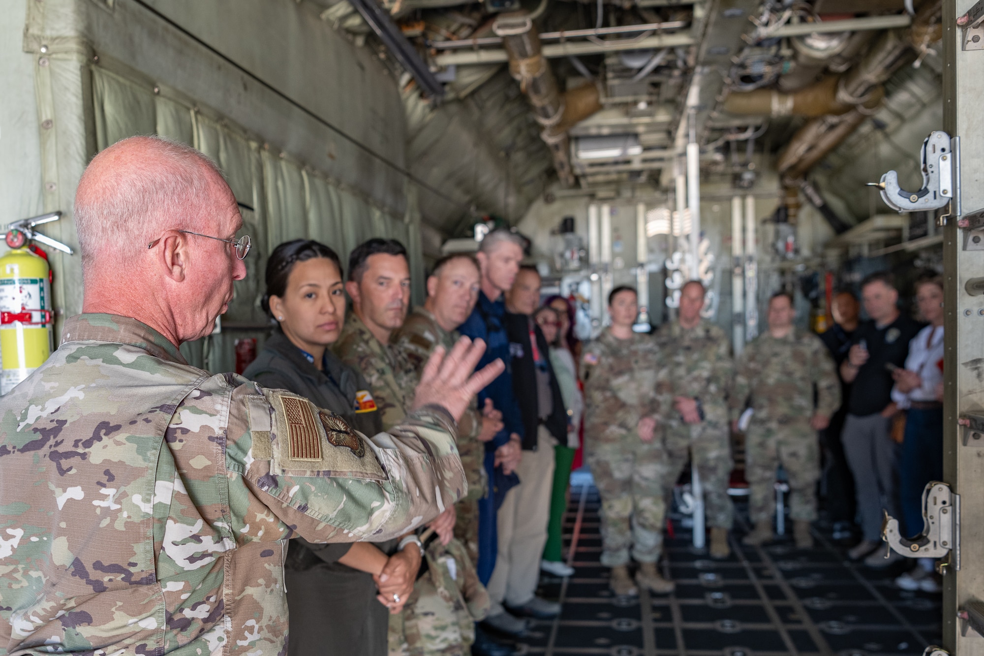 A servicemember gestures to personnel in the back of a military aircraft.