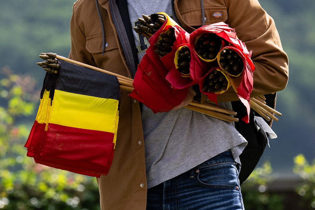 A close-up shot of a person in a jacket and jeans carrying bundles of Belgian flags under both of their arms.