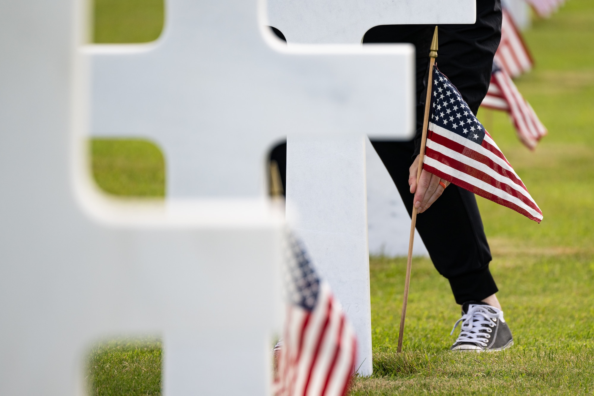 A close-up shot of a hand placing an American flag in front of a limestone cross headstone