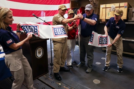 Cmdr. Raymond Miller IV, center left, commanding officer of Arleigh Burke-class guided-missile destroyer USS Bainbridge (DDG 96), and Mr. Christopher Plamp, Chief Operating Officer, United Service Organizations, cut a ribbon in the hangar bay in honor of the ship’s new USO unstaffed entertainment center, May 22, 2025. Bainbridge is a part of Carrier Strike Group 12, which provides combatant commanders and America’s civilian leaders multi-domain power to deter adversaries, underpin American security and economic prosperity, and project global power. (U.S. Navy photo by Mass Communication Specialist Seaman Cesar Licona)