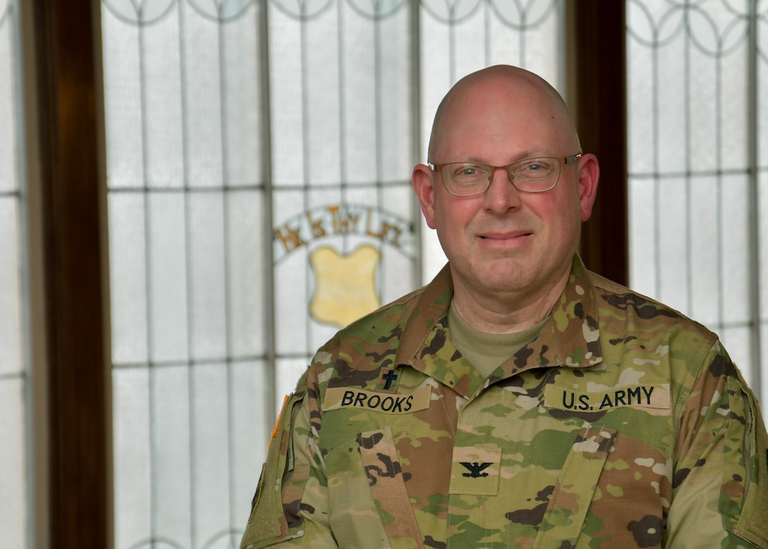 A man in an Army uniform stands looking at the camera.