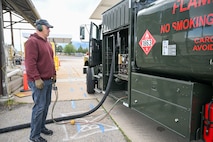 a man stands beside a fuel truck with pump in hand to defuel the truck