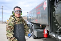 an airman looks at the camera, standing by a fuel truck wearing goggles