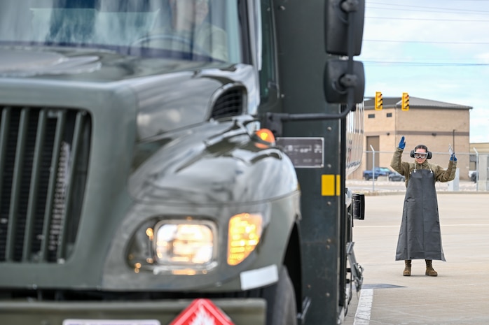 a female airman standing behind a fuel truck directing it to back up with her hands