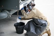 a female airman collects a fuel sample into a jar