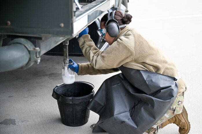 a female airman collects a fuel sample into a jar