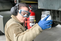 A female wearing goggles looks at a fuel sample in a jar