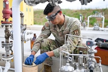 An Airman collects a fuel sample into a jug