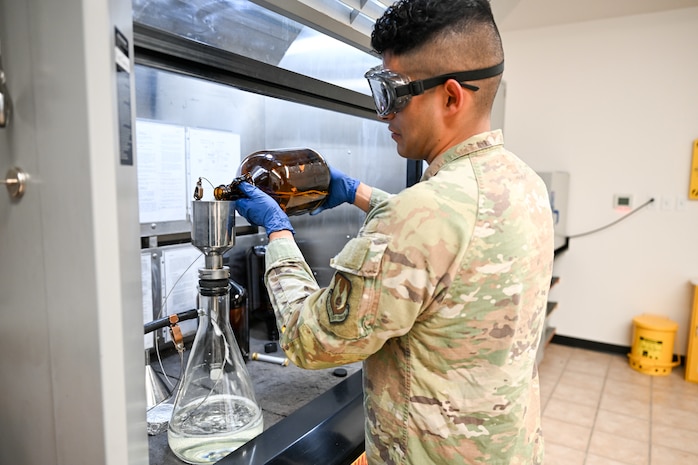 An airman pours a fuel sample into a beaker