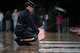 A U.S. Army Soldier wearing a dark blue ceremonial uniform with raincoat is kneeling over at the Tomb of the Unknown Soldier and placing a small U.S. flag at one of the three crypts.