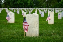 There is a small U.S. flag placed in front of each tombstone in Arlington National Cemetery, which includes rows and rows of white tombstones amid bright green grass.