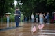 A U.S. Army Soldier wearing a ceremonial uniform with raincoat is standing at attention on a black mat surrounded by wet pavement while maintaining the watch at the Tomb of the Unknown Soldier, which has three small U.S. flags placed over the three crypts.