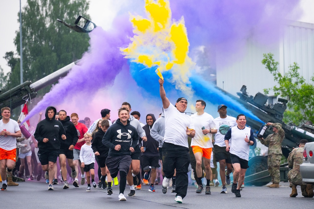 A group of people run under blue, purple and yellow smoke.