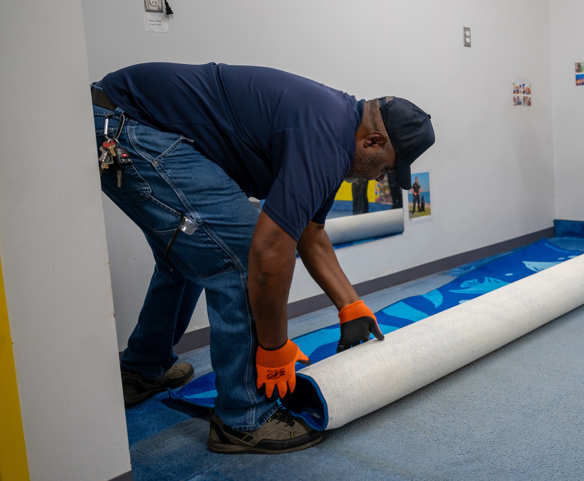 Photo of a volunteer in civilian clothing bending over to unroll a carpet.