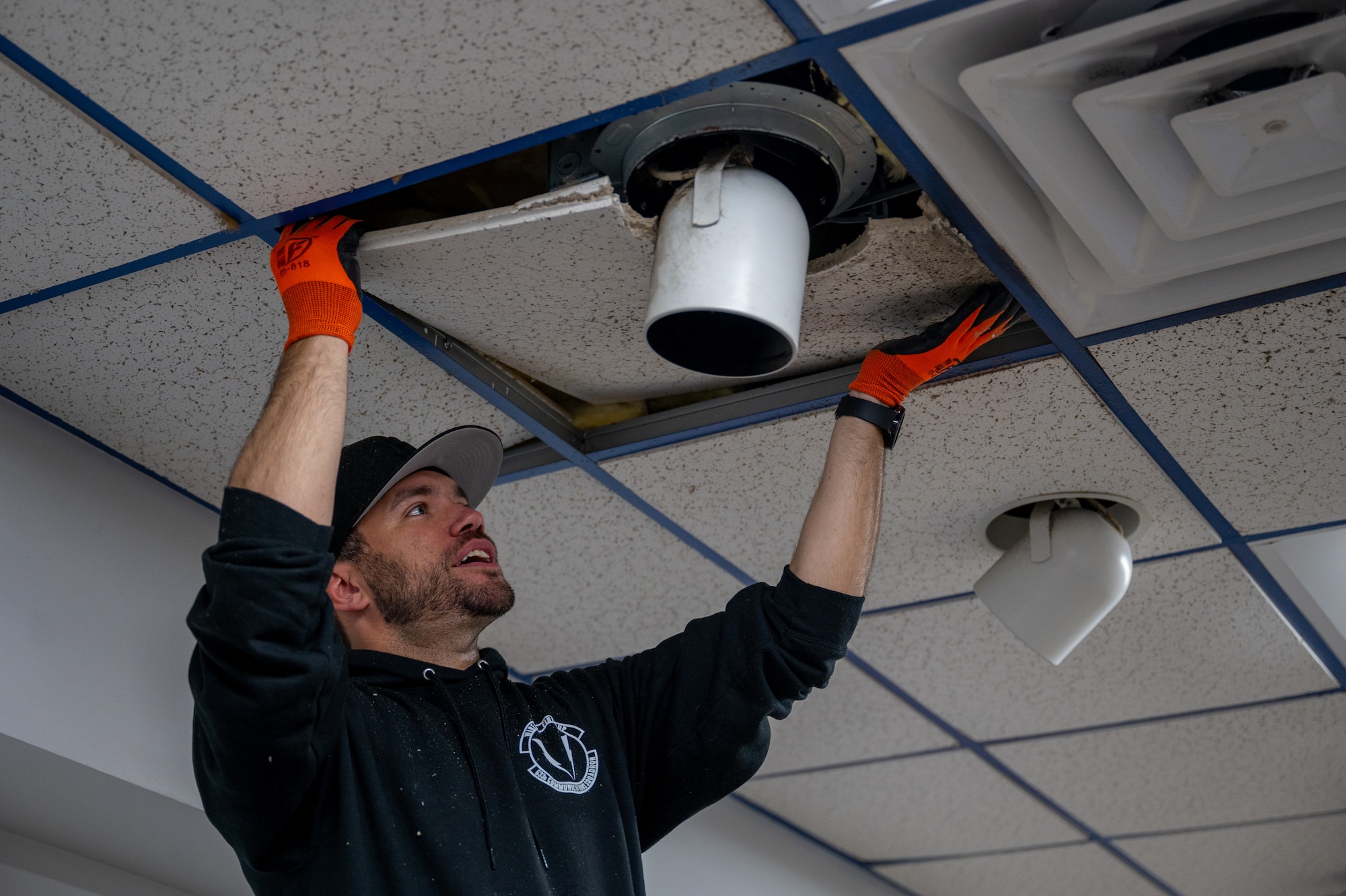 Photo of an Airman in civilian clothing reaching above his head to pull down a ceiling tile.