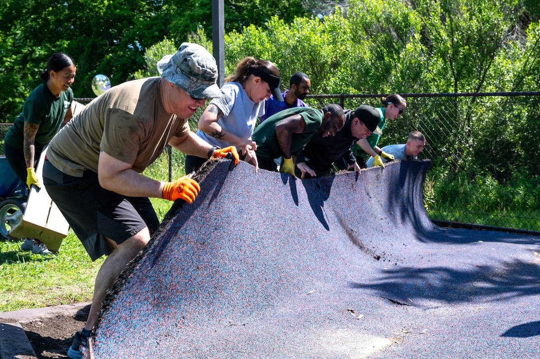 Photo of multiple airmen rolling up outdoor flooring material.