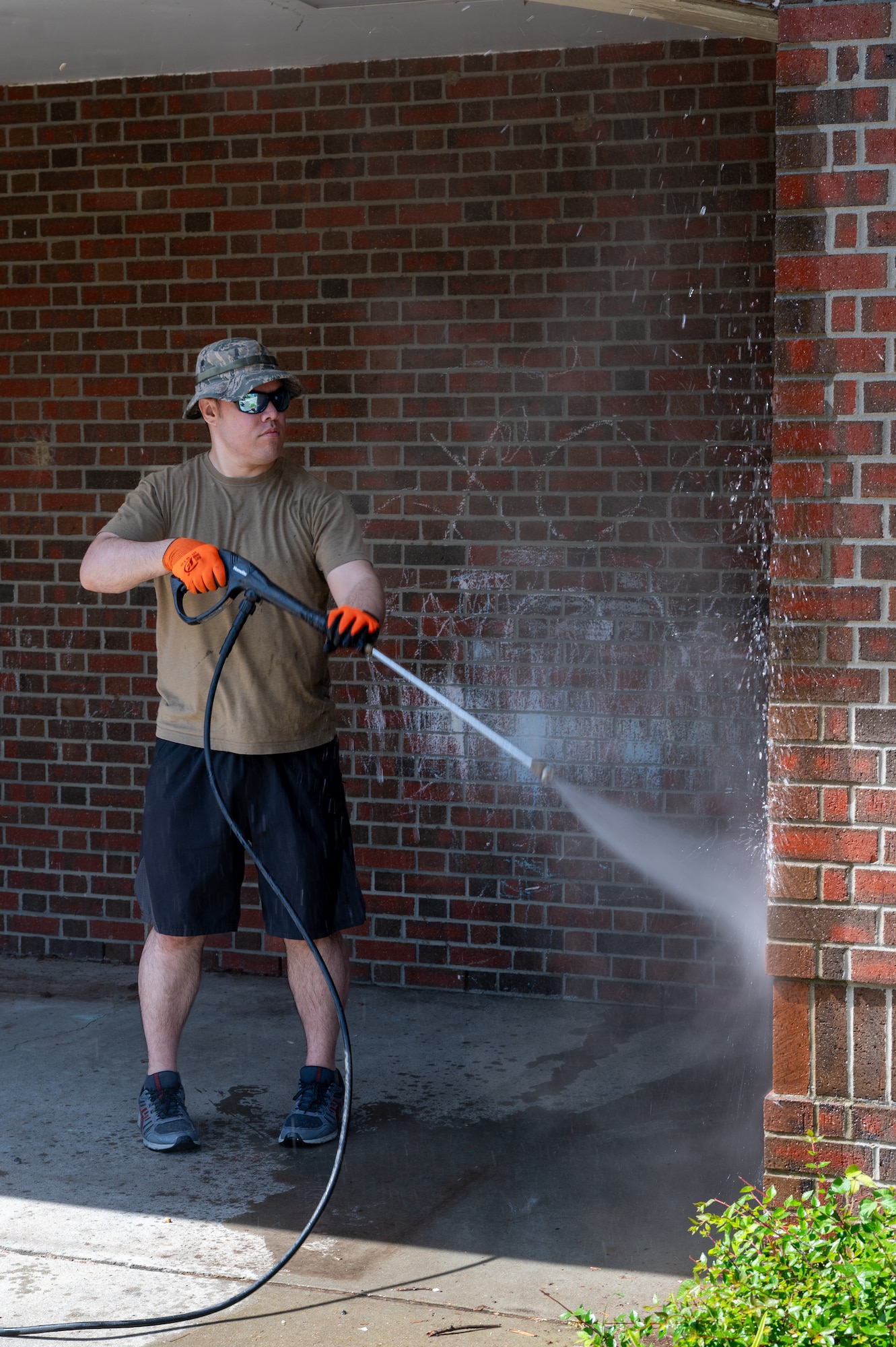Person shown pressure washing the side of a brick building.
