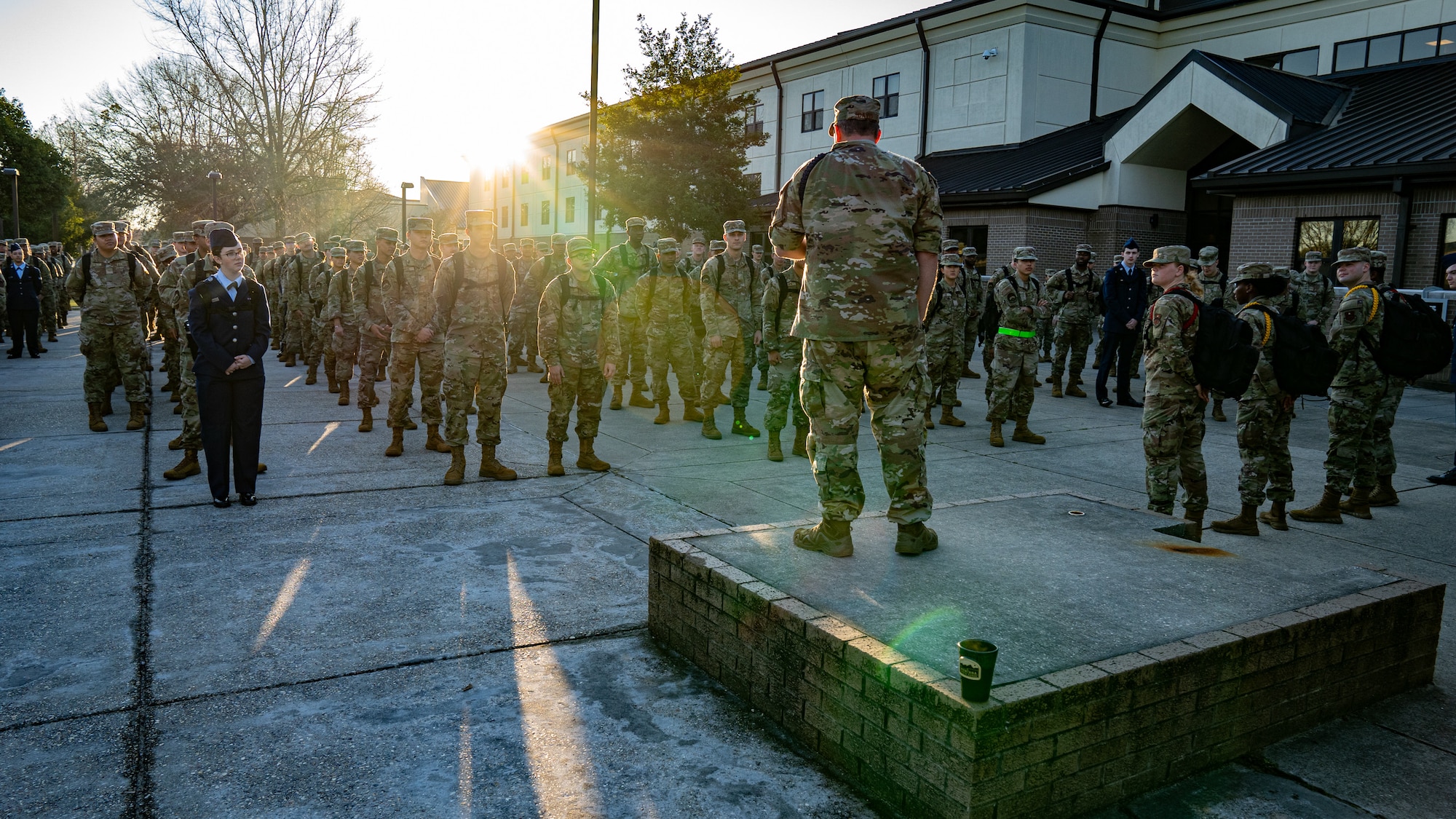 A man in military uniform stands in front of Air Force trainees outside.