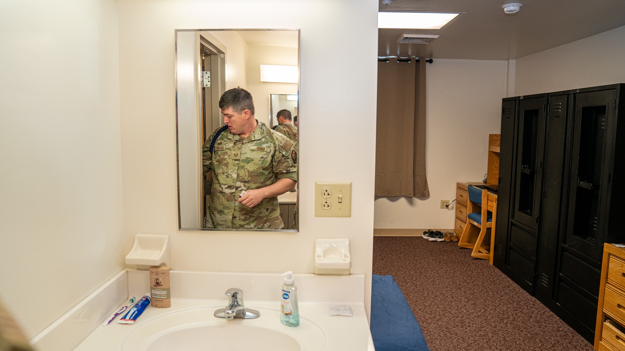 A man in military uniform stands in front of a bathroom mirror inspecting it for cleanliness.