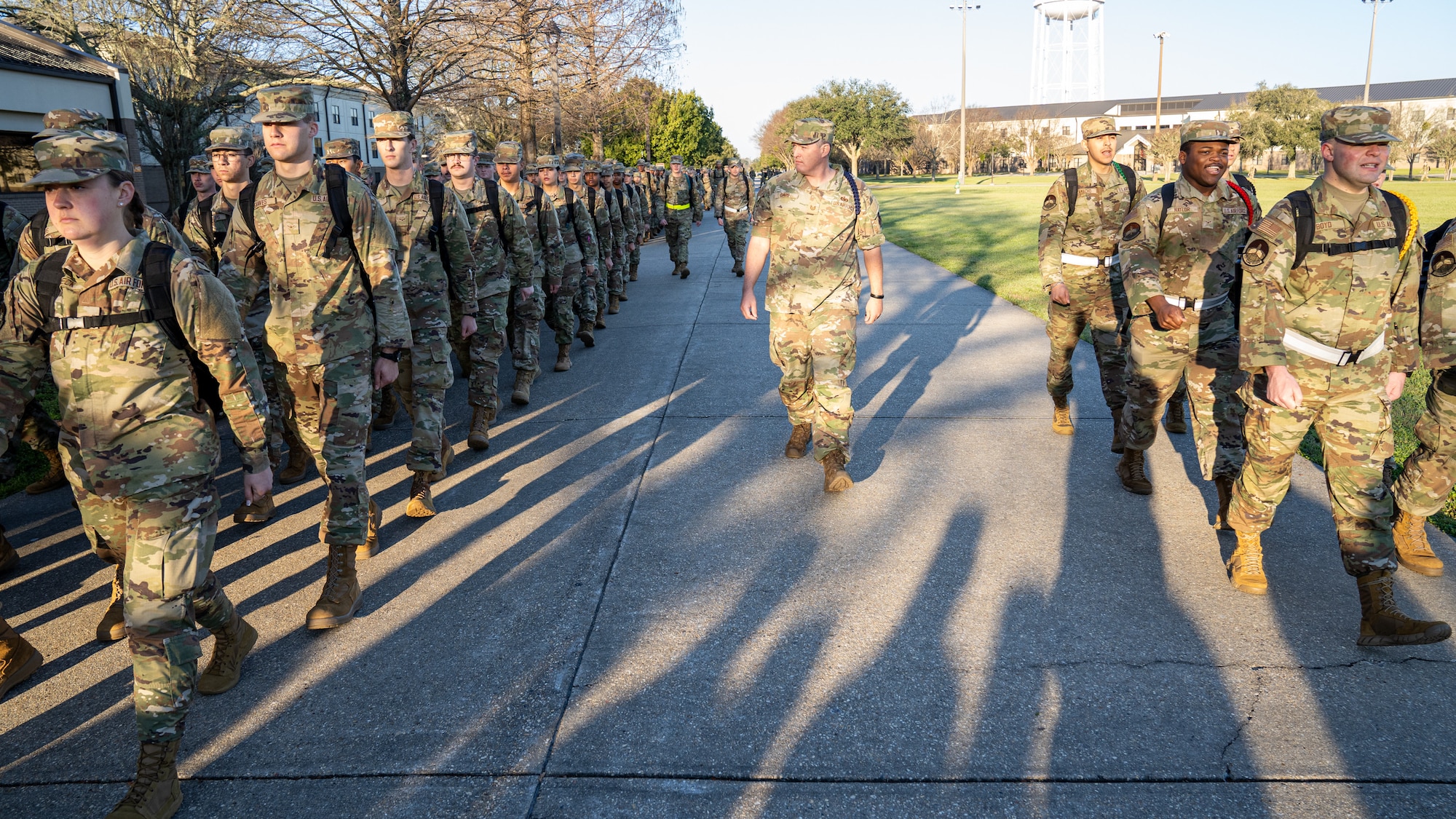 A man in military uniform walks with a group of Air Force trainees while they march.