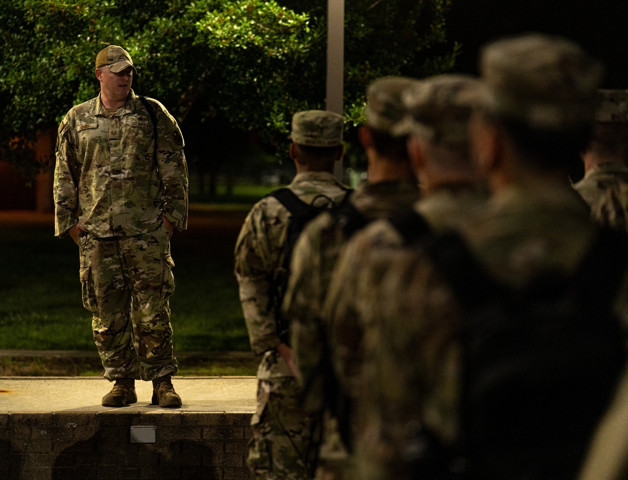 A man in uniform stands in front of a group of Air Force tech trainees giving instruction.