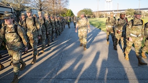 A man in military uniform walks with a group of Air Force trainees while they march.