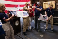 Cmdr. Raymond Miller IV, center left, commanding officer of Arleigh Burke-class guided-missile destroyer USS Bainbridge (DDG 96), and Mr. Christopher Plamp, Chief Operating Officer, United Service Organizations, cut a ribbon in the hangar bay in honor of the ship’s new USO unstaffed entertainment center, May 22, 2025. Bainbridge is a part of Carrier Strike Group 12, which provides combatant commanders and America’s civilian leaders multi-domain power to deter adversaries, underpin American security and economic prosperity, and project global power. (U.S. Navy photo by Mass Communication Specialist Seaman Cesar Licona)