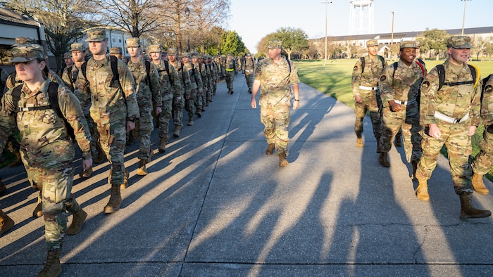 A man in military uniform walks with a group of Air Force trainees while they march.