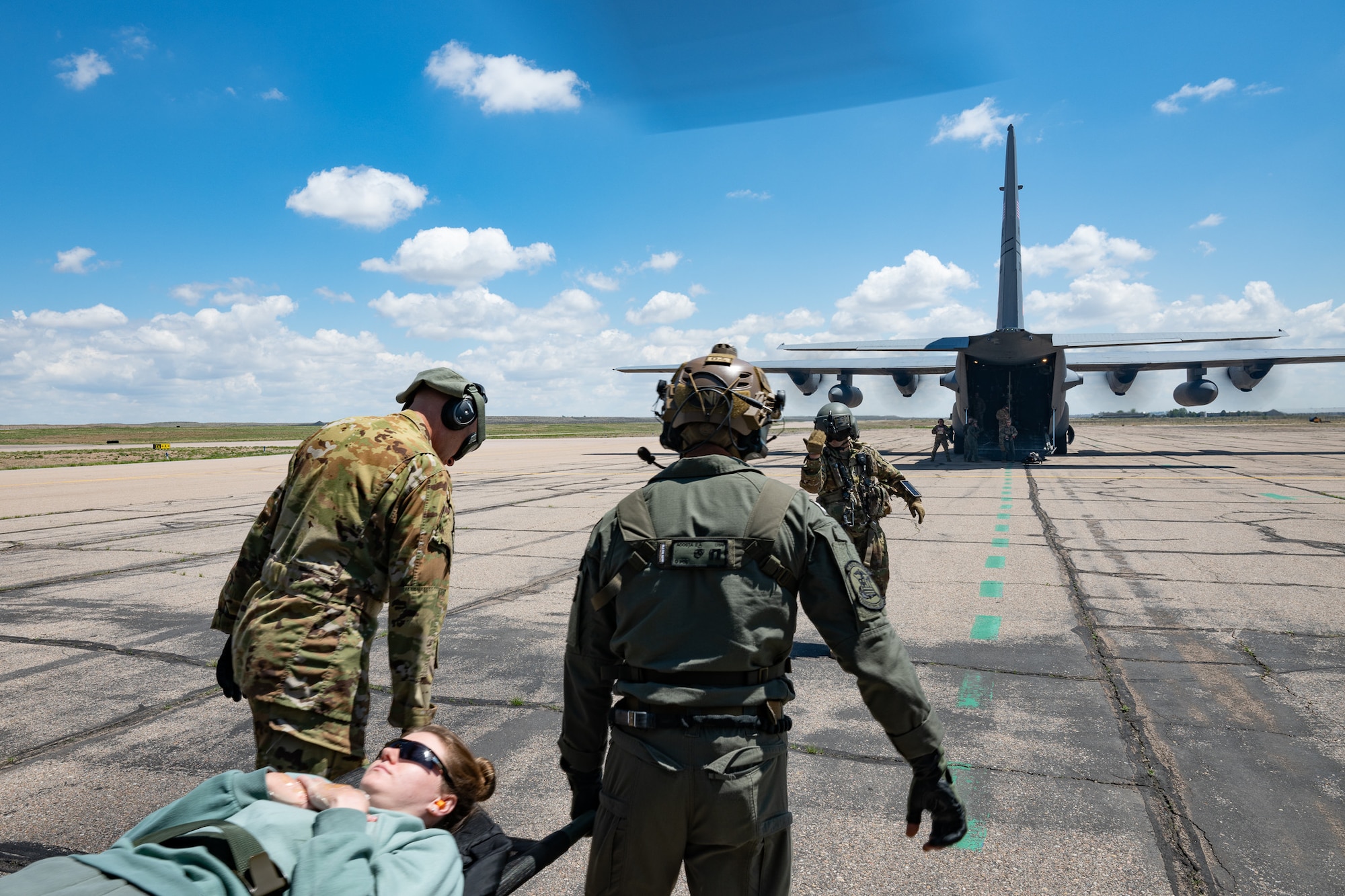 A team carrying a litter patient approaches a military aircraft with its engines running.